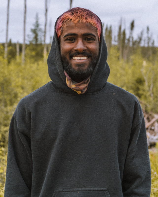 Person wearing a black hoodie with a colorful headband in a forest setting