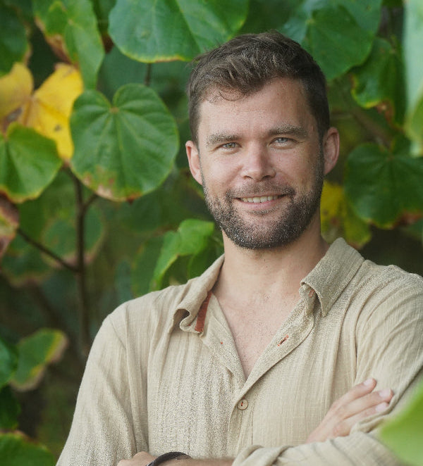 Matt McKernan in beige shirt standing among green leaves